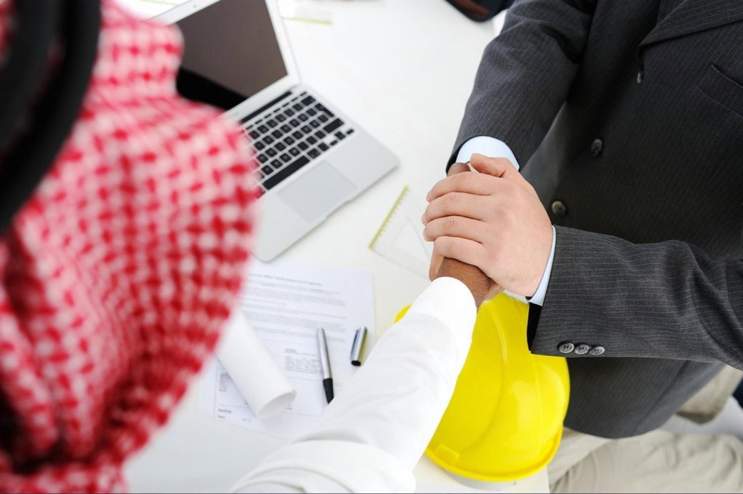 Arab businessman and Western investor shaking hands over a contract and laptop
