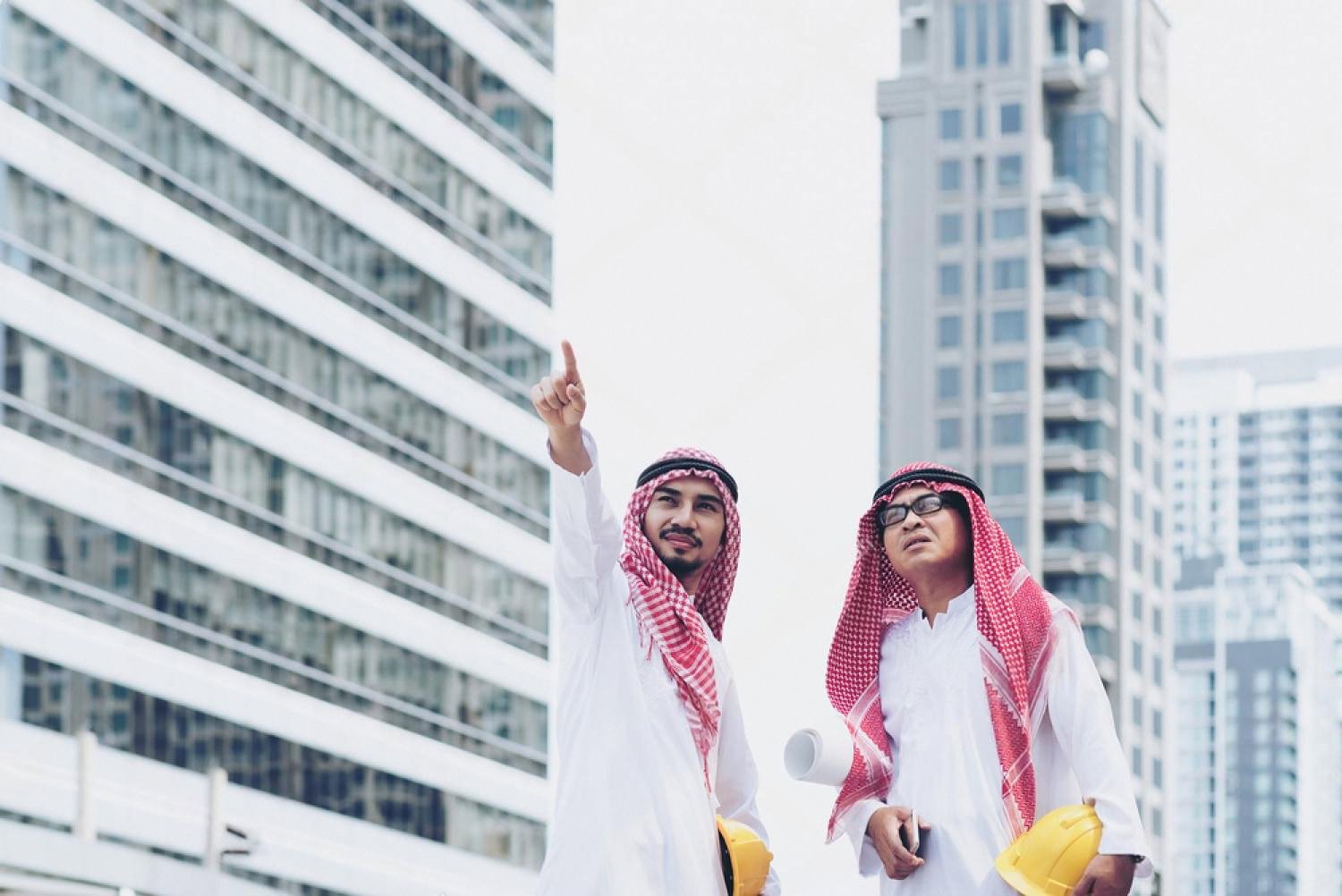 Two businessmen in traditional Gulf dress planning a project in front of UAE skyscrapers